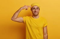 frustrated-adult-male-shows-gun-pistole-keeps-fingers-near-temple-frowns-face-distressed-with-much-work-wears-yellow-hat-t-shirt