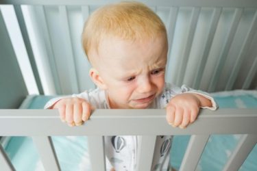 Worried cute baby standing in crib