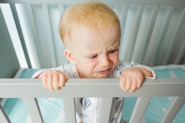 Worried cute baby standing in crib